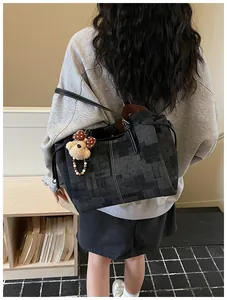 Détail du sac cabas en denim gris foncé avec anses en cuir et petit ours décoratif