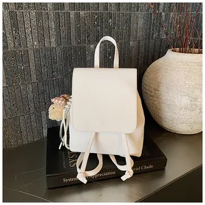 Detail of a minimalist cream white leather mini backpack with a cute bear charm accessory