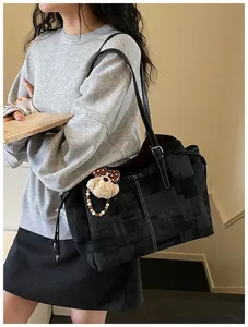 Détail du sac cabas noir avec motif à carreaux et breloque ours en peluche sur la bandoulière