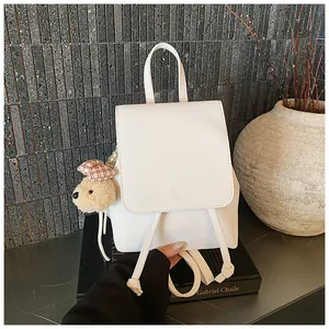 Detailed view of white leather backpack with flap closure, drawstring, and plush bear charm