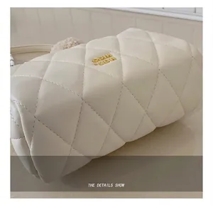 Dettaglio della borsa a cilindro beige con cuciture trapuntate e logo dorato