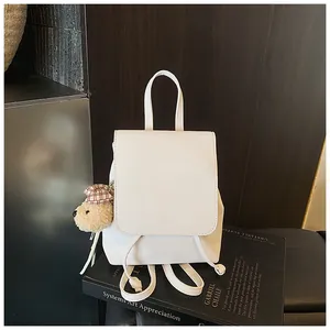 White faux leather mini backpack with a brown plaid bear charm on a dark artistic background