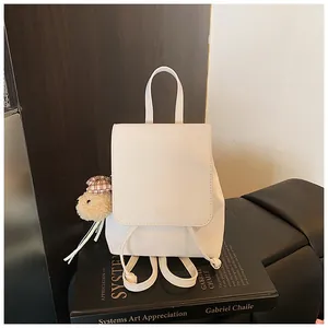 Minimalist white faux leather backpack on black art book with cute bear keychain charm