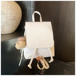 Detail of white minimalist backpack with faux leather finish and a cute plush bear charm