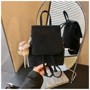 Detail view of black matte drawstring backpack with plush bear charm and flap closure
