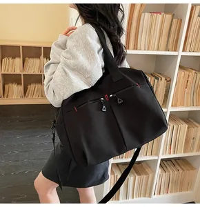 Dettaglio borsa da viaggio nera con cuciture rosse e tasche con zip indossata da uomo