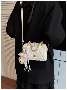 Dettaglio borsa trapuntata crema con logo dorato, catena e ciondolo di peluche carino