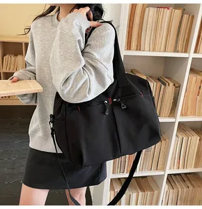 Dettaglio della tracolla regolabile e cuciture rosse sulla borsa da viaggio in tela nera