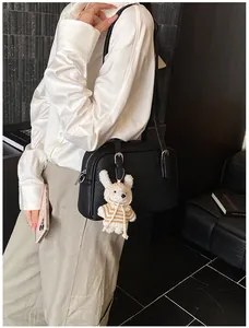 Close-up of black lychee grain leather crossbody bag with a white plush bunny charm