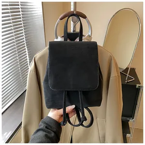 Detailed macro view of a black suede mini backpack featuring a flap and drawstring closure