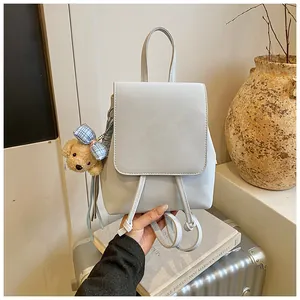 Detail of light gray matte leather backpack featuring a cute plush bear charm on the side