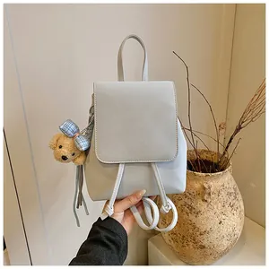 Detail of light gray PU leather mini backpack featuring a plush bear charm and magnetic flap