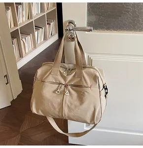 Dettaglio borsa da viaggio in tela beige appesa con cerniere metalliche e cuciture rosse