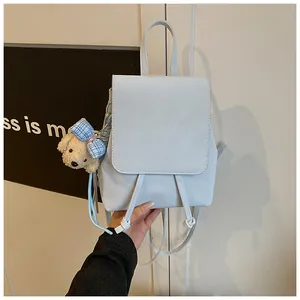 Close-up of a white minimalist backpack with drawstring closure and cute teddy bear charm
