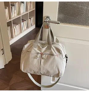 Dettaglio borsa da viaggio in tela con doppie tasche a zip appesa a una porta bianca