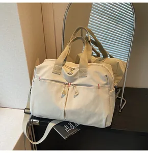 Dettaglio del borsone da viaggio beige con doppie cerniere e accenti di cucitura rossi
