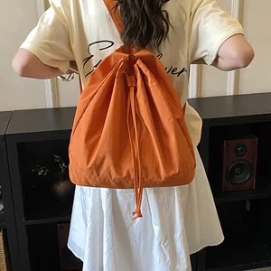 Rear view of model wearing a large orange drawstring backpack made of canvas material