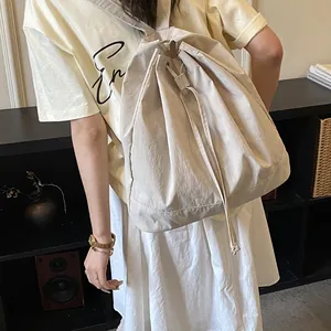 Detail of beige drawstring canvas backpack showing side drape and large capacity on model