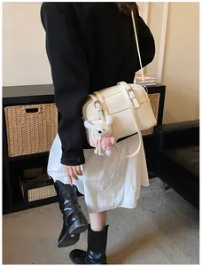 Detail of cream lychee texture crossbody bag with metal buckles and pink knit rabbit charm