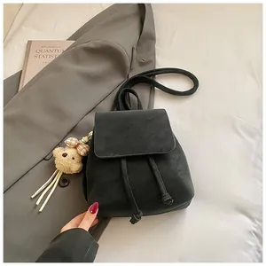 Detail of a matte black faux leather backpack with drawstring closure and plush bear charm