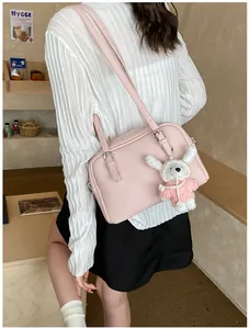 Detail of pink lychee textured leather crossbody bag with a cute white rabbit pendant