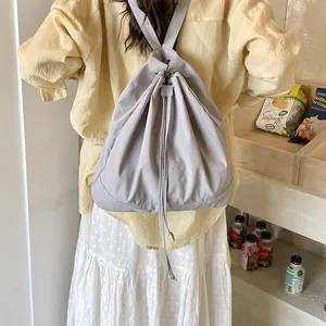 Back view of light grey drawstring backpack worn with casual shirt and pleated skirt