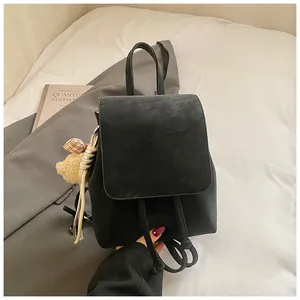 Detail of matte black minimalist backpack featuring a flap closure and cute plush bear charm