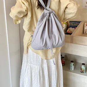 Close-up of light gray minimalist drawstring backpack worn by model in casual setting