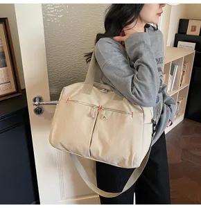 Dettaglio borsa da viaggio in tela beige con due tasche frontali e cuciture rosse rinforzate