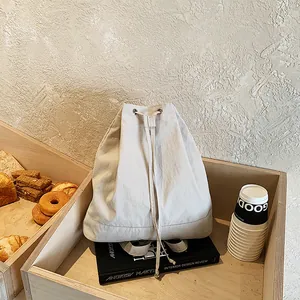 Minimalist beige canvas drawstring backpack shown on a wooden tray in a lifestyle setting