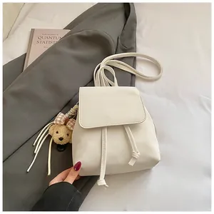 Detail of a beige mini backpack featuring drawstring closure and a cute plush bear charm