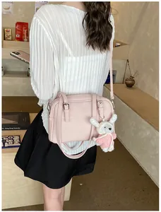 Pink litchi texture crossbody bag with cute teddy bear charm on model's shoulder