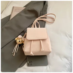 Pink PU leather backpack with drawstring closure and cute bear plush charm on bed