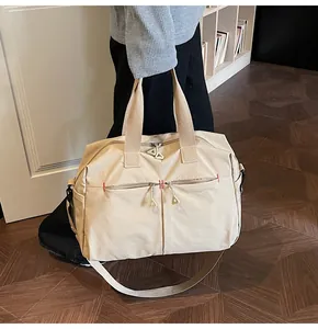Dettaglio borsa da viaggio beige con zip metalliche triangolari e cuciture rosse a contrasto
