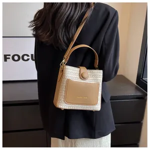 Detail of a straw bucket bag with leather pocket and shoulder strap worn by a model