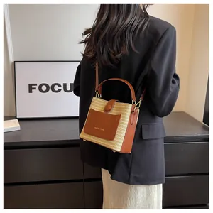 Detail of hand-woven straw bucket bag featuring a brown leather pocket and gold brand logo