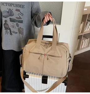 Dettaglio borsa da viaggio in tela kaki con cuciture rosse su valigia bianca