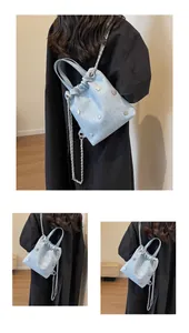 Détail du sac seau en jean bleu clair avec rivets argentés et bandoulière en chaîne