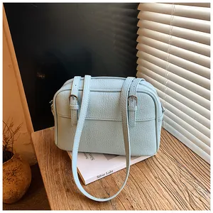 Detail of light blue lychee pattern leather shoulder bag on white books with sunlight
