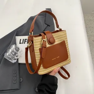 Minimalist straw bucket bag with dark brown leather trim and golden logo detail