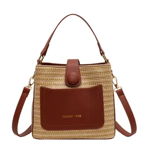 Minimalist straw bucket bag with brown leather trim and Mandan Verse logo on white background