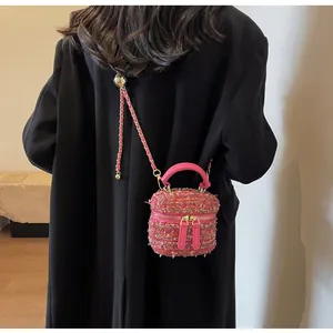 Detail der rosa Tweed-Mini-Beuteltasche mit goldener Kette auf schwarzer Jacke