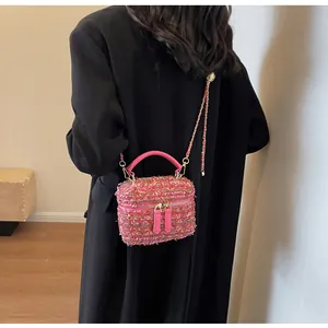 Detailansicht der rosa Tweed-Handtasche mit goldener Kette auf schwarzem Mantel