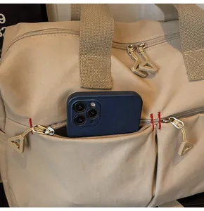 Dettaglio borsa da viaggio in tela kaki con cuciture rosse e tasca anteriore per cellulare