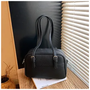 Detail of black pebbled leather crossbody bag with silver buckles on a wooden table