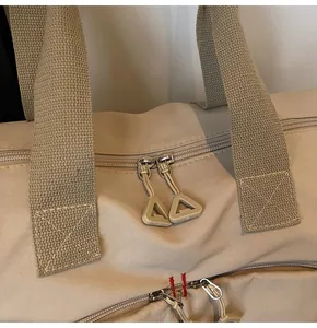 Dettaglio borsa da viaggio in tela beige con doppia cerniera e ampi manici in tessuto