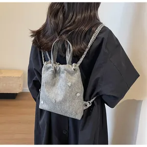 Détail d'un sac à dos gris en tissu avec clous en cœur argentés et bandoulière chaîne