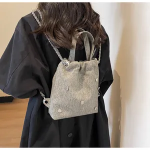 Détail d'un sac à dos en denim gris avec rivets en cœur et chaînes argentées sur un mannequin