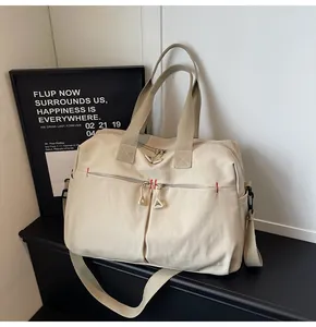 Dettaglio della borsa da viaggio in tela beige con tasche a zip e cuciture rosse