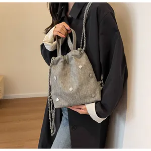 Gros plan du sac seau en denim gris orné de clous en cœur et de bandoulières chaînées